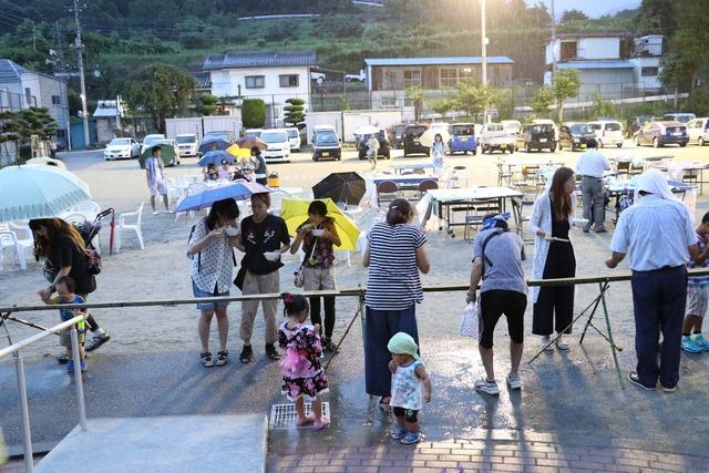 雨の中、傘をさしながら流しそうめんをする人々の写真