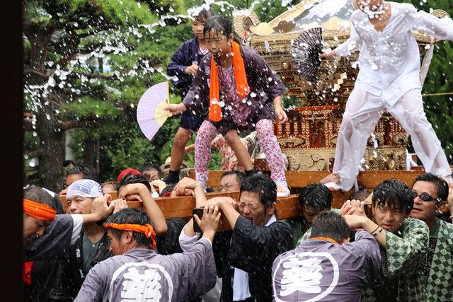 女の子が神輿の上にたち、水をかけられている写真