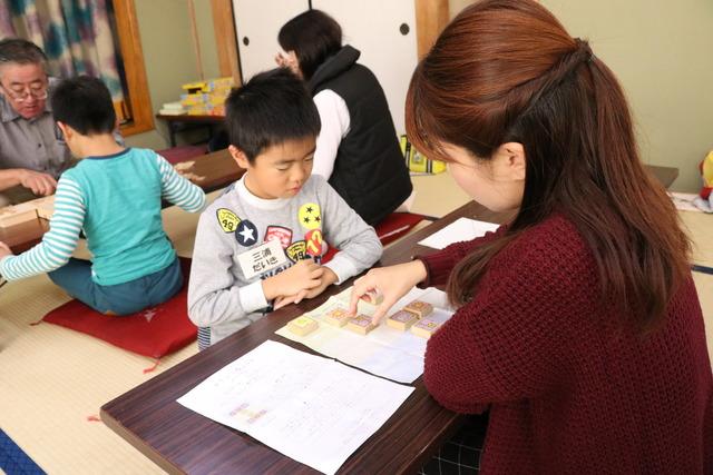 紙の上で木でできた四角い駒を動かし駒の動き方を学んでいる男の子の写真