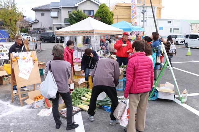 人たちがフリーマーケットで野菜などを買っている写真