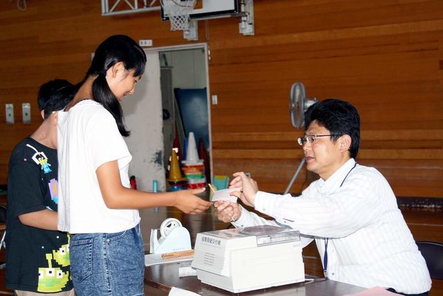 竜王西小学校の体育館にて女子児童に本物同様の選挙の投票用紙を配る写真