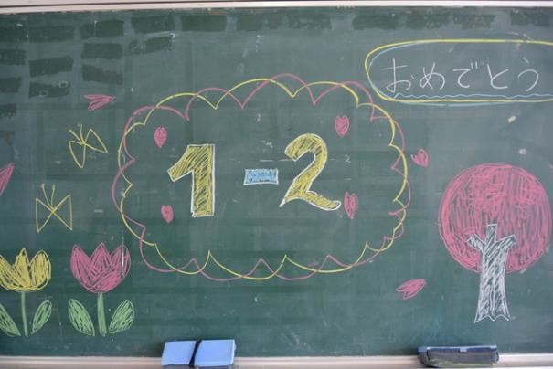 「1年2組」「おめでとう」の文字とチューリップ、桜の絵などが描かれた黒板の写真