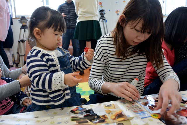 写真を台紙に糊で貼り付けしている参加者の女性と小さなお子さんの写真