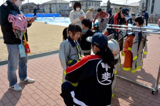 子ども用の消防服を着せてもらっている女の子の写真