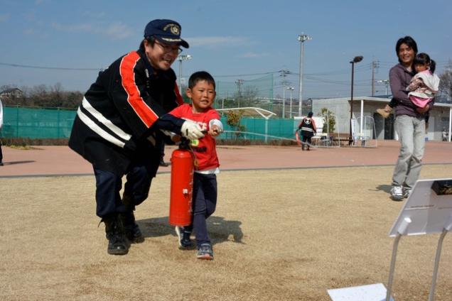 消防団員と共に消火器を構えている男の子の写真