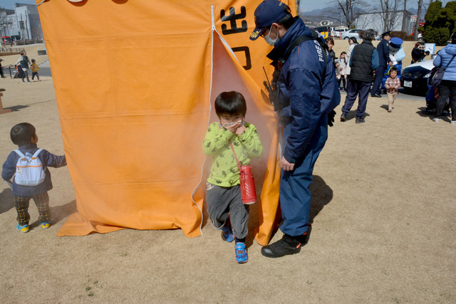 煙が充満したテントの中から、ハンカチで鼻と口を押えて出てくる子どもの写真