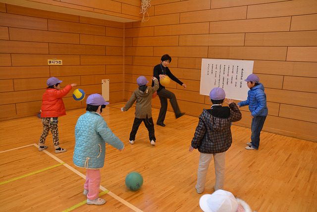 体育館で先生とまりつきの練習をしている子どもたちの写真