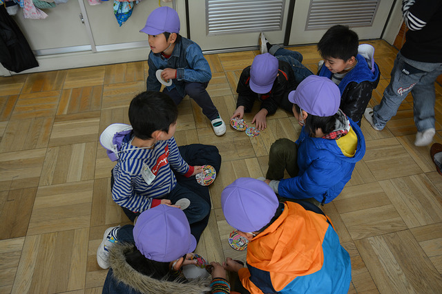 教室の床に座ってめんこで遊ぶ児童の写真