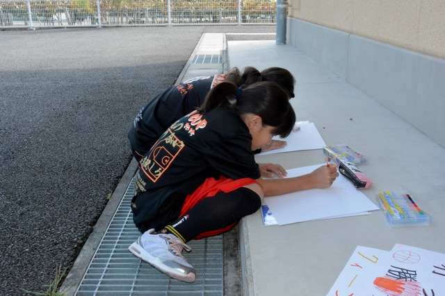 体育館の外で、画用紙に目標などを書き込む子どもたちの写真