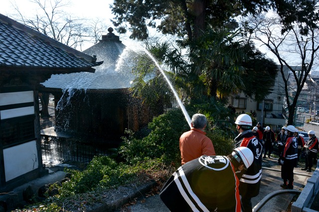 消防士と住民が寺に向けて消火栓からの放水訓練をしている写真