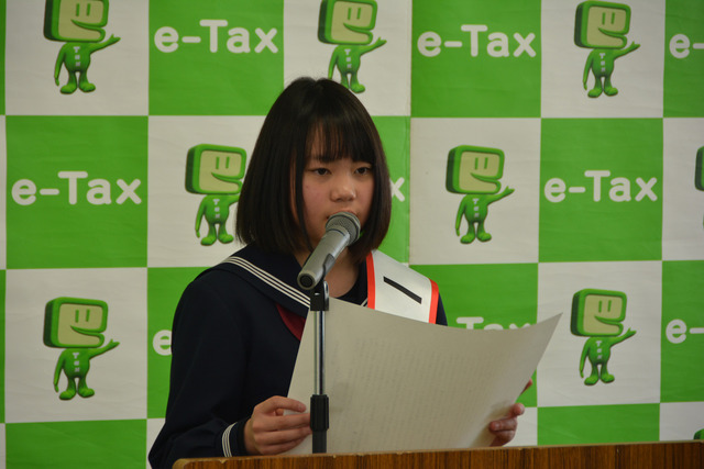 税務署職員の前で、訓示として受賞作文「消費税の謎」を朗読する平賀さんの写真