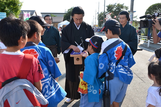 山縣大弐、従者に扮した一行があおばこども園から山縣神社まで「福銭」を来場者に配りながら行進を行っている写真