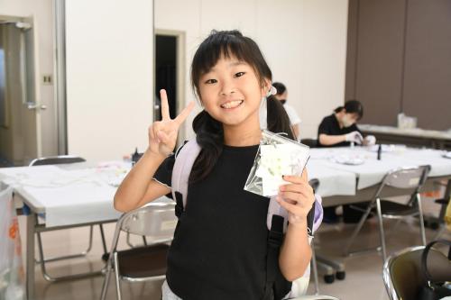 完成したアクセサリーを手にピースする子どもの写真