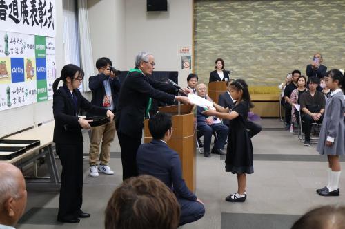 表彰状を受け取る小学校低学年の女子