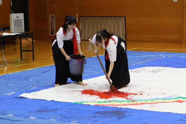 大きな紙に筆で書く高校生の写真