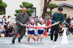 一本の棒を４人d横一列になってもって走る競技をする子どもと大人