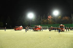 市消防団訓練総見、グラウンド照明に照らされるポンプ車