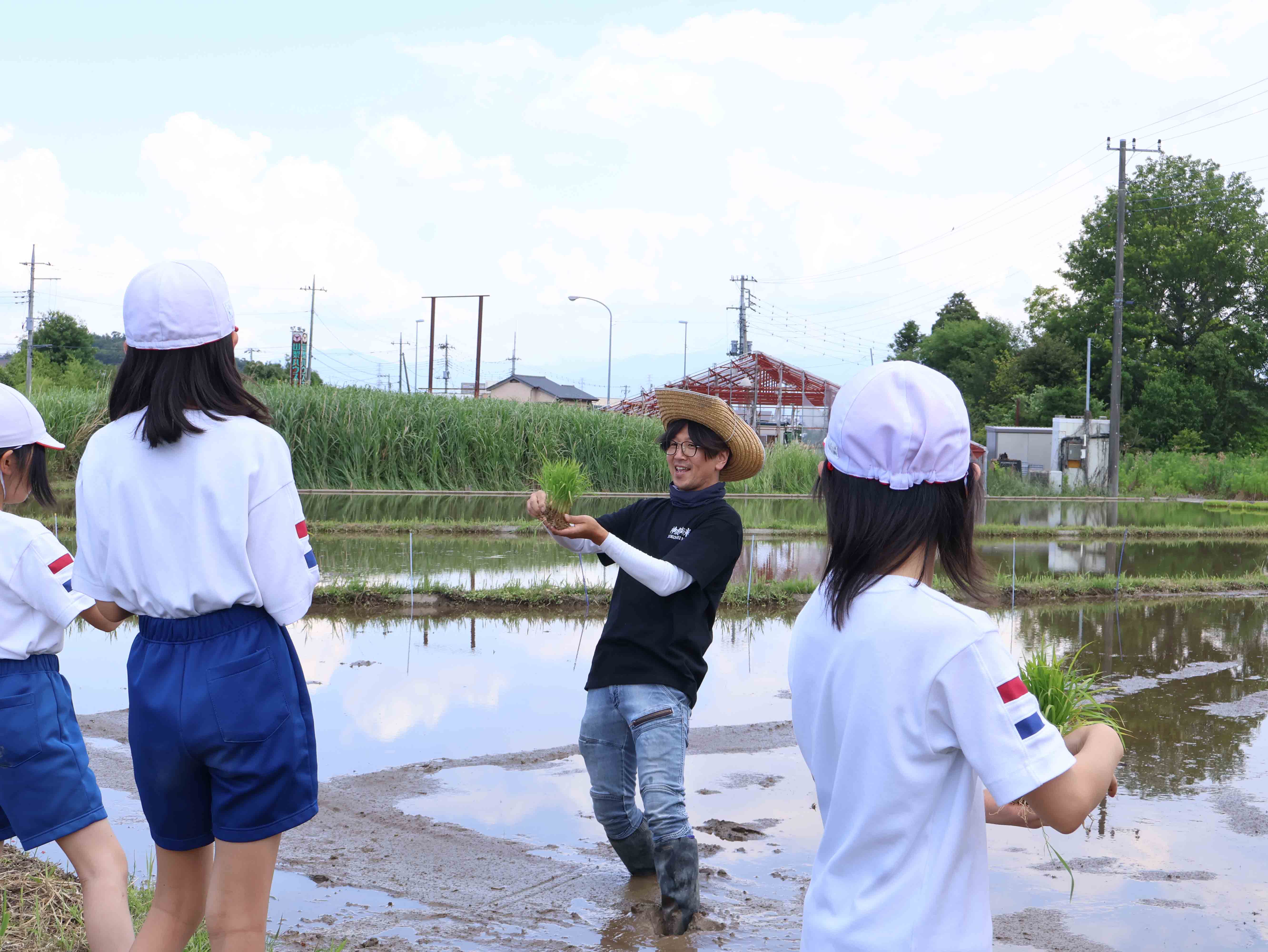 田んぼで田植えの説明をする農家の方と児童1