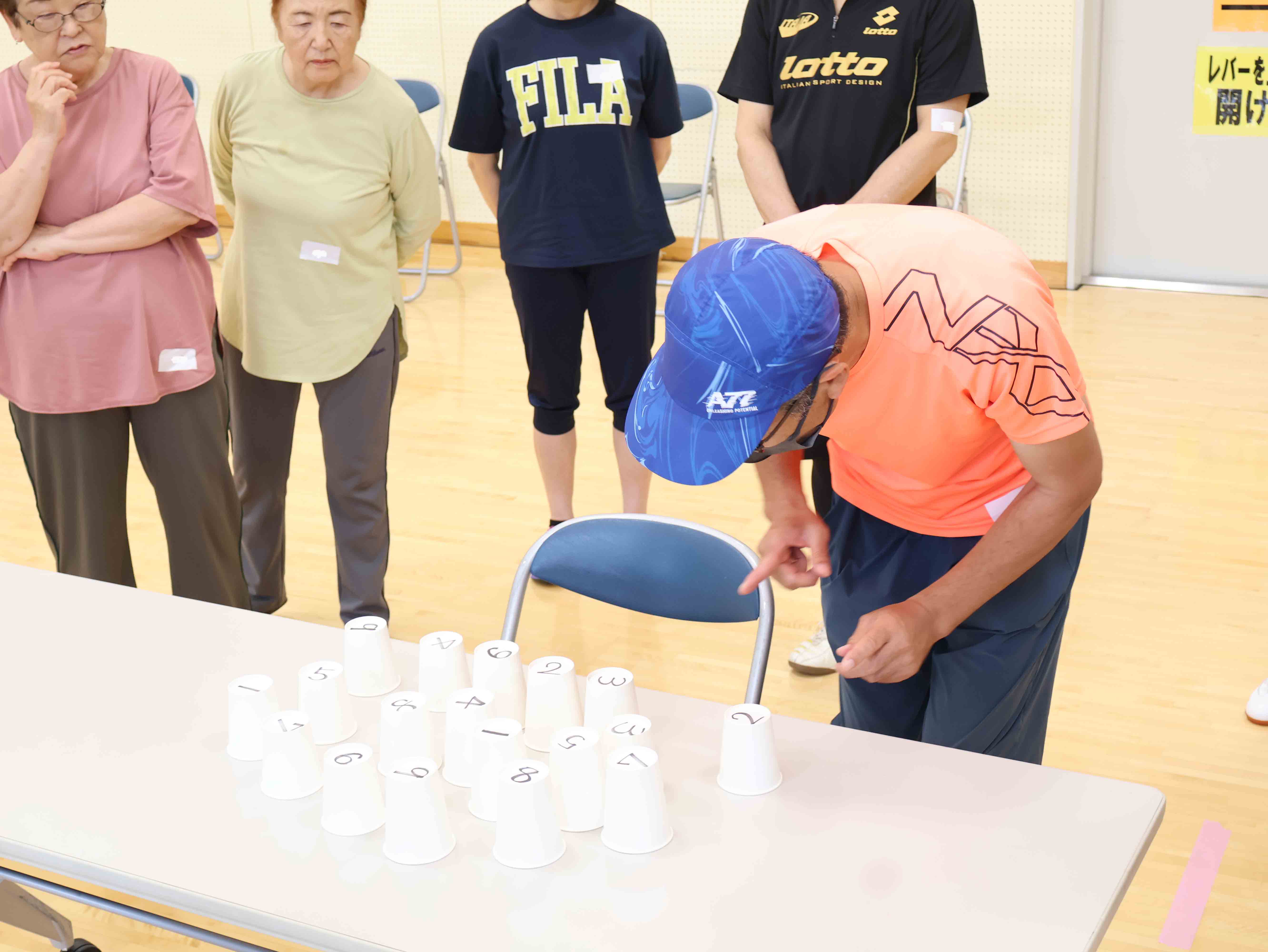 数字の書かれた紙コップを見せながらゲームの説明をする講師